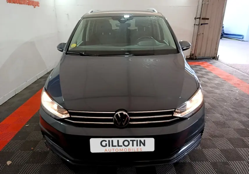 Vue avant d'un Volkswagen Touran gris foncé 2023 avec phares allumés dans un garage fermé.