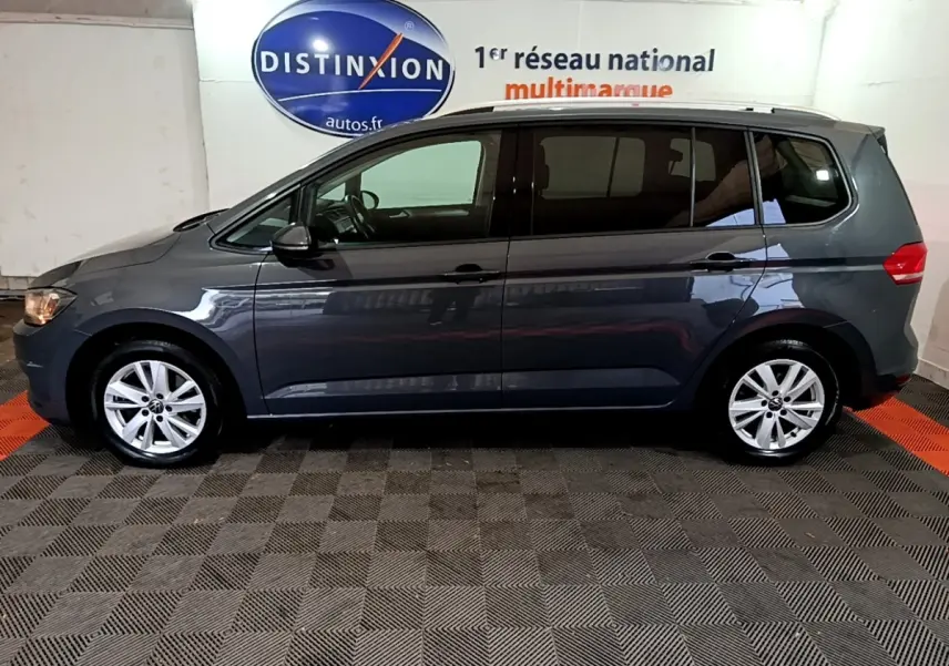 Profil côté gauche d'un Volkswagen Touran gris foncé 2023 stationné en intérieur avec jantes alliage visibles.