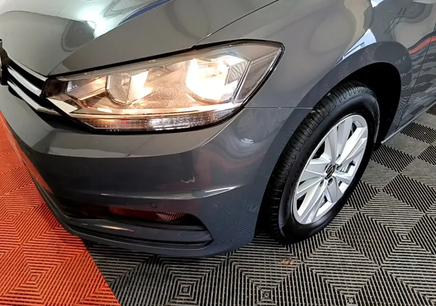 Gros plan sur l'avant droit gris foncé du Volkswagen Touran 2023 avec phare allumé et jante aluminium.