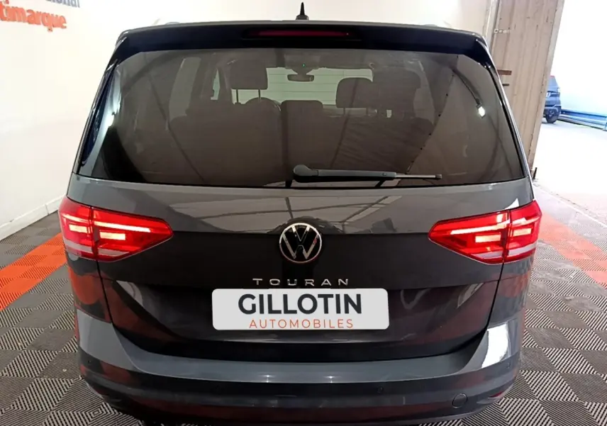 Vue arrière d'un Volkswagen Touran gris foncé 2023 avec feux LED allumés et logo VW visible.