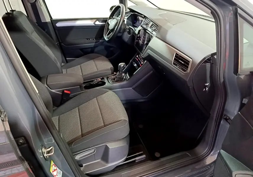 Intérieur avant droit du Volkswagen Touran gris foncé 2023, sièges tissu et tableau de bord avec écran tactile.