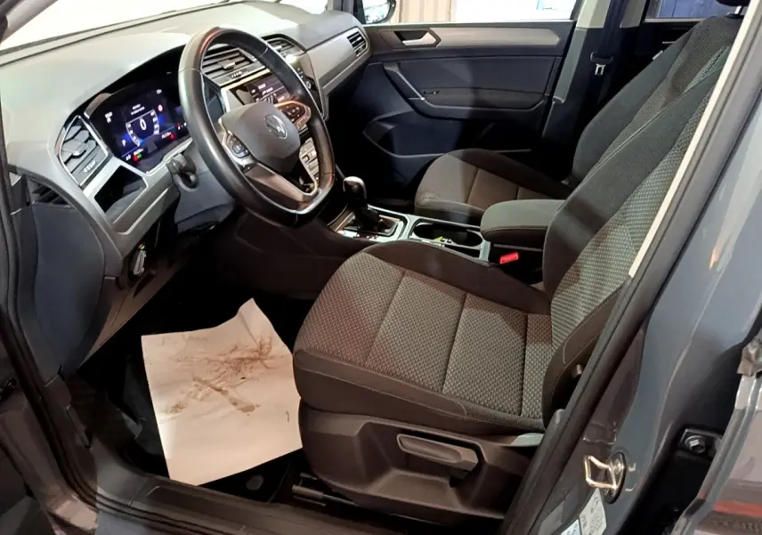 Vue intérieure côté conducteur du Volkswagen Touran gris foncé 2023, volant cuir et tableau de bord digital visible.