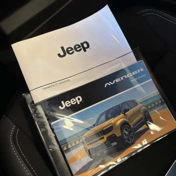 Vue rapprochée des manuels Jeep posés sur un siège noir avec surpiqûres blanches, sans véhicule visible.