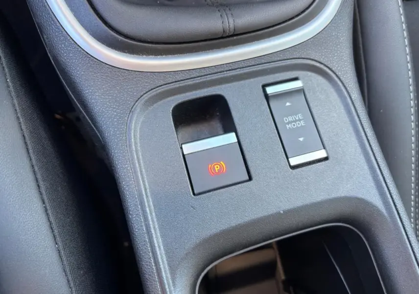 Gros plan sur la console centrale noire du Jeep Avenger 2024 montrant le frein de parking électrique et le bouton Drive Mode.