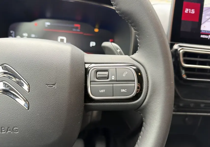 Gros plan sur le volant cuir noir du Citroën C5 Aircross 2025, avec commandes multifonctions et tableau de bord numérique en arrière-plan.