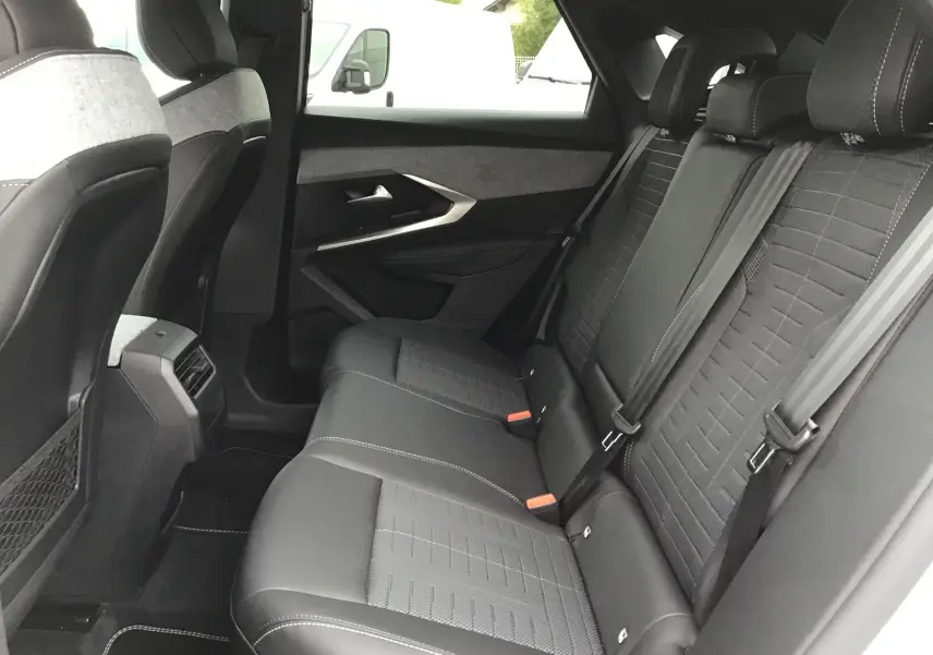 Vue intérieure arrière côté droit du Peugeot 3008 1.2 Hybrid 145 GT+ blanc Okenite avec sièges noirs en tissu et cuir, appuie-têtes visibles.