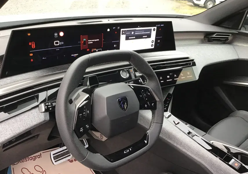Vue intérieure du poste de conduite du Peugeot 3008 blanc Okenite, avec tableau de bord numérique et volant compact GT.