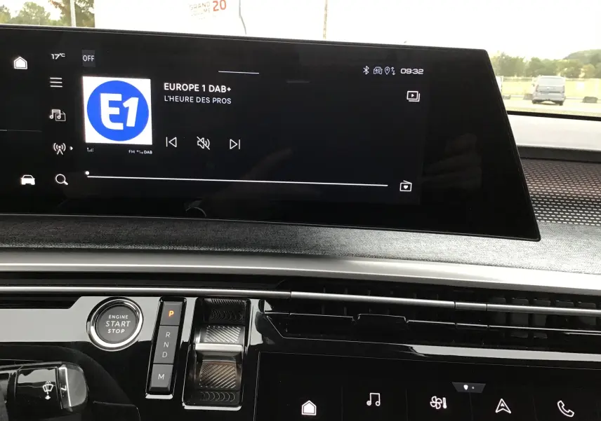 Vue intérieure du tableau de bord du Peugeot 3008 blanc Okenite, avec écran tactile central affichant la radio Europe 1 et commandes modernes.