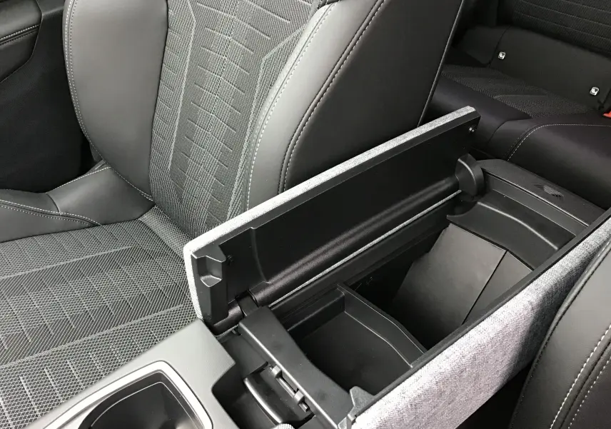 Vue rapprochée de l'accoudoir central ouvert et siège avant en tissu gris et cuir noir dans le Peugeot 3008 hybride 2026.