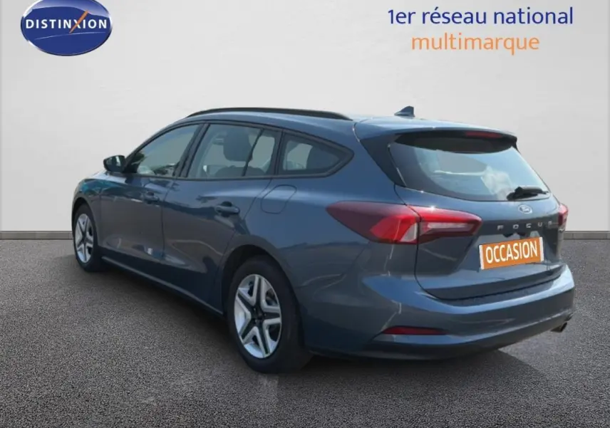Vue 3/4 arrière droite d'une Ford Focus SW bleu foncé avec barres de toit et jantes classiques 16 pouces.