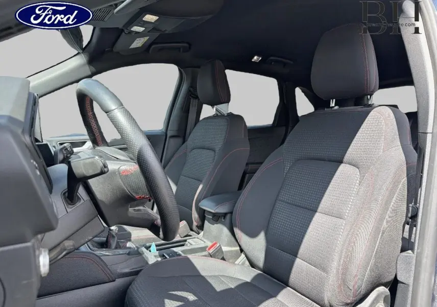 Vue intérieure côté conducteur du Ford Kuga 2020, sièges sport noirs avec surpiqûres rouges et volant cuir multifonction.