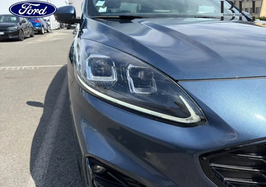 Gros plan sur l'avant droit bleu métallisé du Ford Kuga 2020, mettant en valeur le phare LED et la calandre noire.