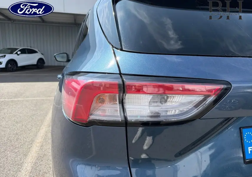 Gros plan sur le feu arrière gauche d’un Ford Kuga bleu Abysse 2020, avec reflet du ciel sur la carrosserie.
