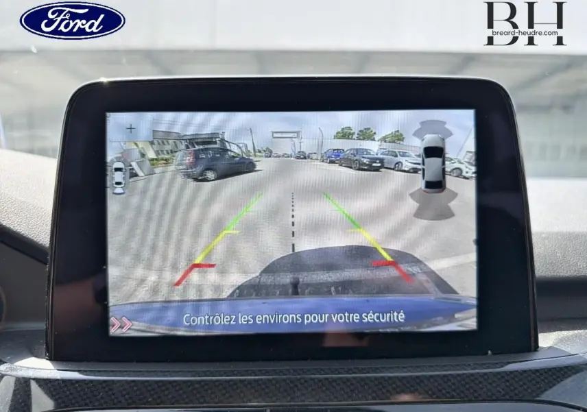 Écran tactile intérieur montrant la caméra de recul avec vue arrière et lignes de guidage du Ford Kuga bleu.