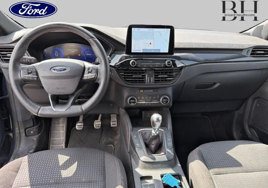 Vue intérieure avant du Ford Kuga bleu avec tableau de bord noir, volant cuir multifonction et levier de vitesse manuel.