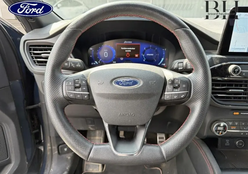 Vue rapprochée du volant cuir sport noir avec surpiqûres rouges du Ford Kuga 2020, tableau de bord digital en arrière-plan.