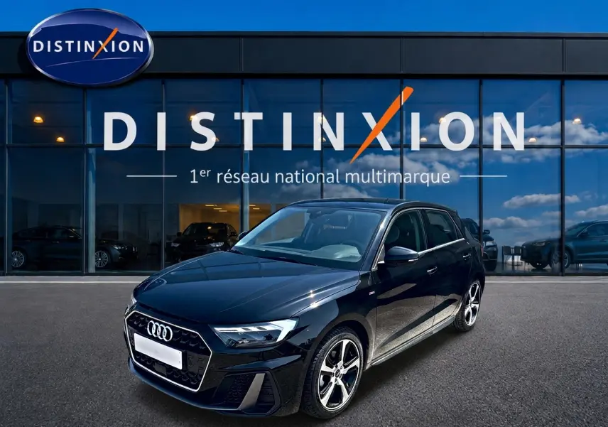 Audi A1 Sportback noir vue 3/4 avant droit, avec jantes alu et calandre hexagonale S line devant un showroom Distinxion.