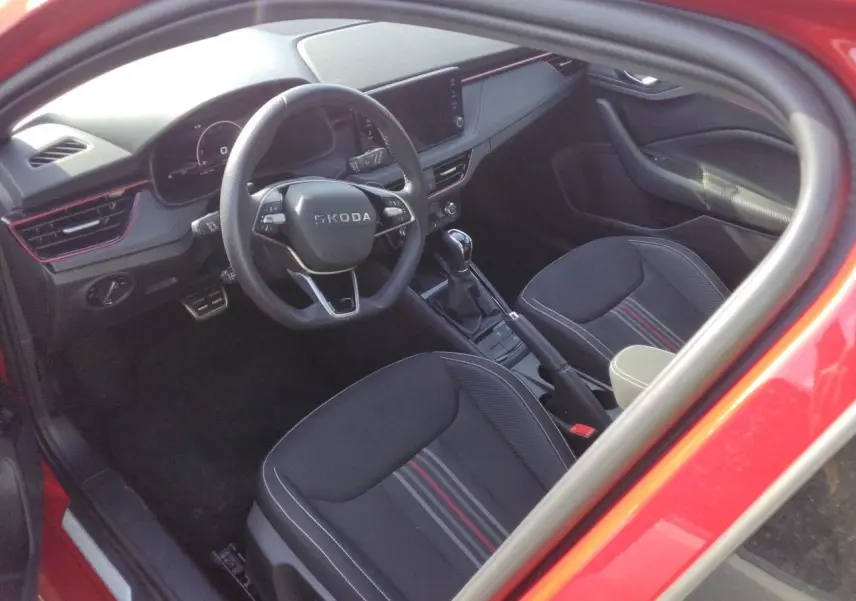 Vue intérieure côté conducteur de la Skoda Scala Monte-Carlo rouge Velvet, volant cuir et sièges noirs à bandes rouges.