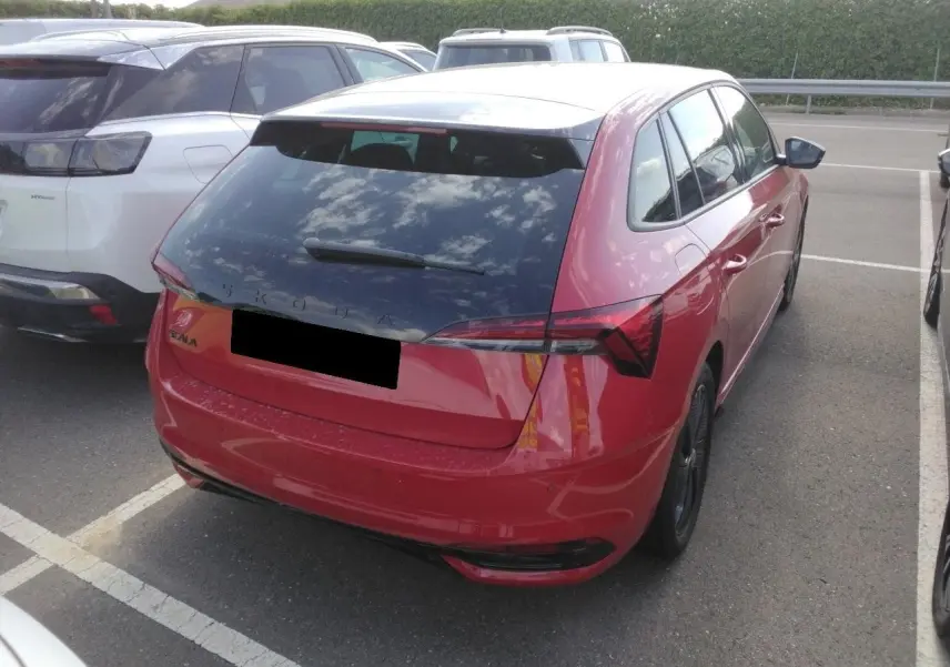 Vue 3/4 arrière droite d’une Skoda Scala rouge Velvet avec toit panoramique et hayon électrique sur parking.