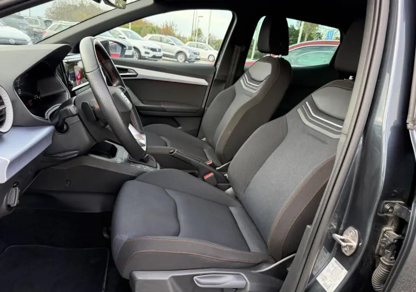 Intérieur de la SEAT IBIZA 2024 vue côté conducteur, sièges tissu gris avec surpiqûres orange et volant multifonction.
