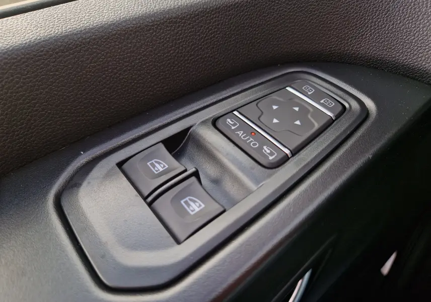 Gros plan sur les commandes de lève-vitres et réglage des rétroviseurs côté conducteur du Nissan Primastar gris urbain.