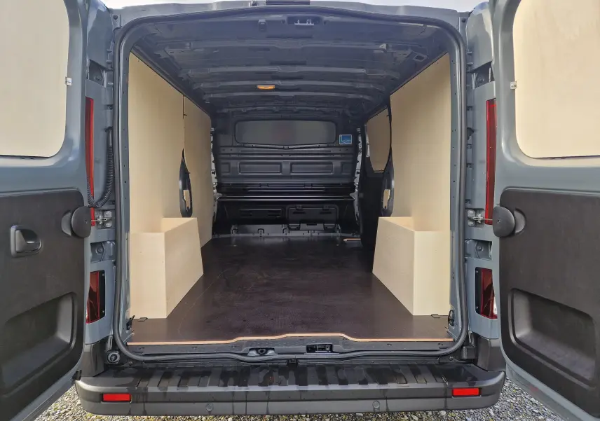 Vue arrière ouverte du Nissan Primastar gris urbain 2025, montrant l'intérieur spacieux avec aménagement bois Pack Cargo.