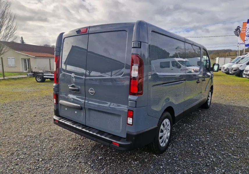 Vue 3/4 arrière droite d’un Nissan Primastar gris urbain 2025, fourgon utilitaire avec portes arrière battantes.