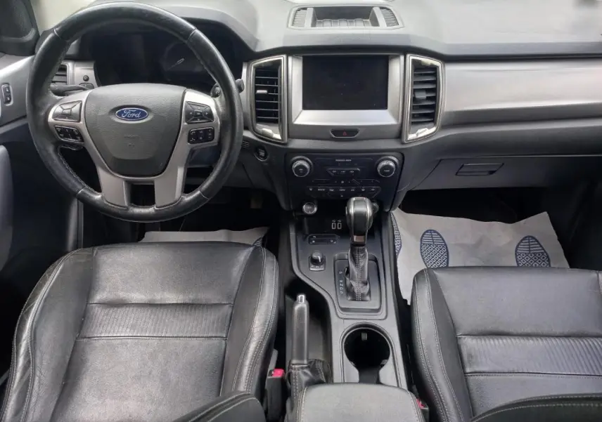 Vue intérieure avant du Ford Ranger 2022, tableau de bord et sièges noirs, volant multifonction et console centrale avec boîte auto.