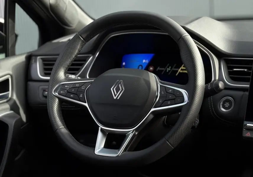 Vue rapprochée du volant noir perforé de la Renault SYMBIOZ 2025 avec tableau de bord numérique bleu en arrière-plan.