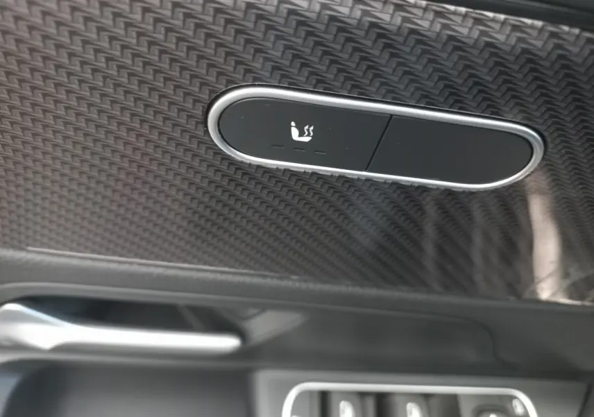 Détail du bouton de chauffage de siège sur la porte intérieure en finition carbone d’une Mercedes Classe A AMG Line noire.