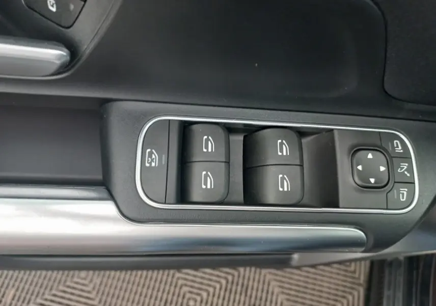Gros plan sur les commandes des vitres et rétroviseurs côté conducteur d'une Mercedes Classe A berline noire.