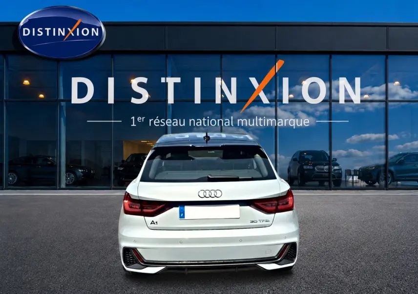 Vue arrière d'une Audi A1 Sportback 30 TFSI gris arrow avec feux LED et becquet arrière, devant une vitrine Distinxion.