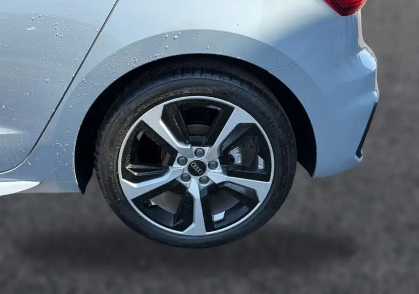 Gros plan sur la roue arrière droite de l'Audi A1 Sportback gris arrow avec jante alu bicolore et carrosserie mouillée.