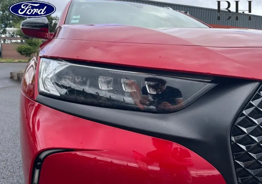 Gros plan sur le phare avant gauche rouge Absolu du DS7 Crossback avec calandre noire et reflets sur la carrosserie.