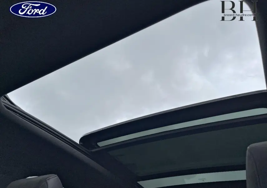 Vue intérieure du toit ouvrant panoramique ouvert du DS7 Crossback Rouge Absolu, montrant le ciel nuageux au-dessus.