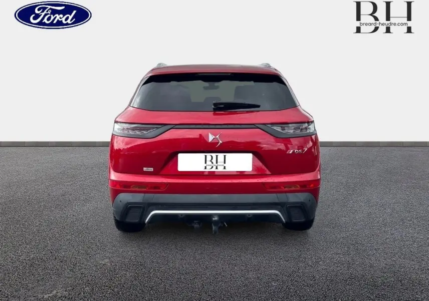 Vue arrière d'un DS7 Crossback rouge Absolu avec feux arrière LED et attelage visible sur sol goudronné.