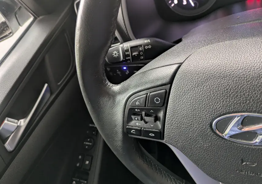 Gros plan sur le volant cuir noir côté gauche du Hyundai Tucson 2020, avec commandes audio et téléphone intégrées.