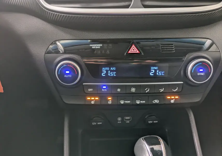 Vue rapprochée de la console centrale noire du Hyundai Tucson 2020, affichant la climatisation automatique et les commandes chauffantes.