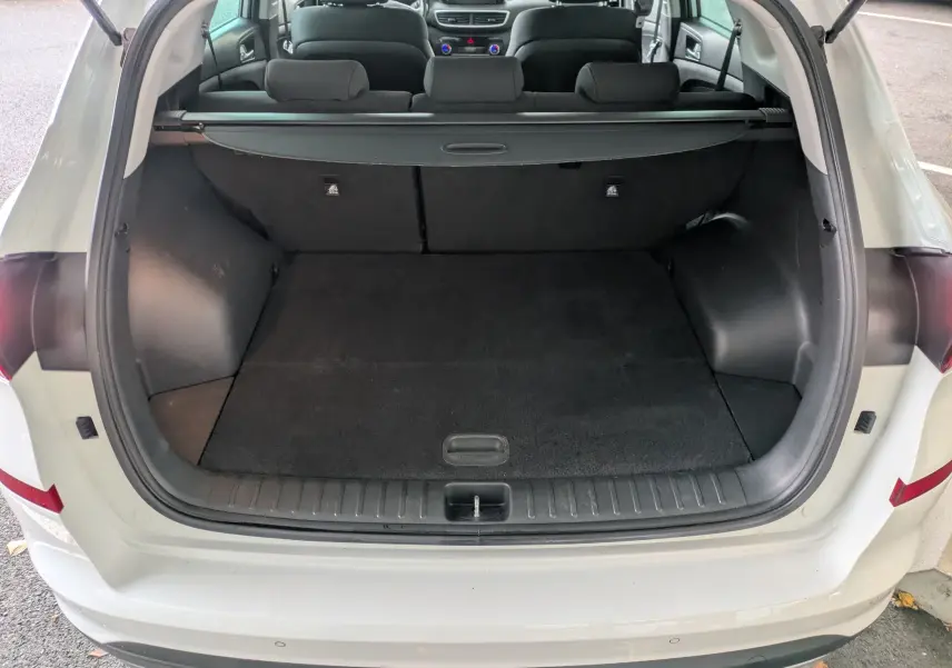 Coffre ouvert vu de l'arrière d'un Hyundai Tucson blanc 2020, montrant un espace de chargement noir et une tablette cache-bagages.