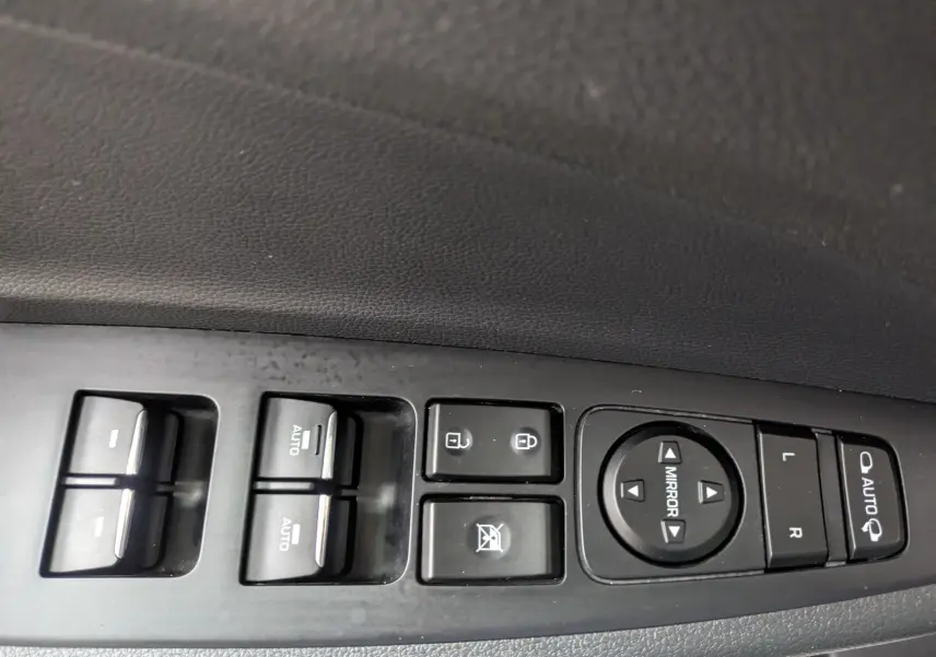 Gros plan sur les commandes de lève-vitres et réglage des rétroviseurs côté conducteur d'un Hyundai Tucson blanc 2020.