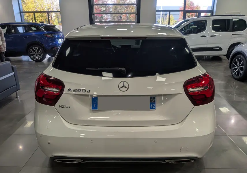 Vue arrière d'une Mercedes Classe A 200d blanche 2016 avec feux rouges et double sortie d'échappement visible en intérieur showroom.