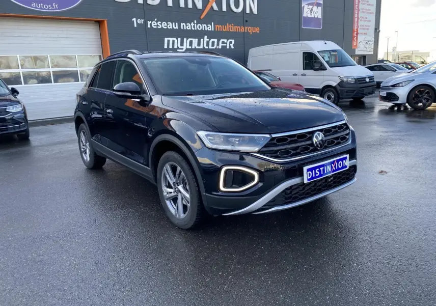 Volkswagen T-Roc noir nacré en 3/4 avant droit, avec feux LED et calandre distinctive sur parking humide.
