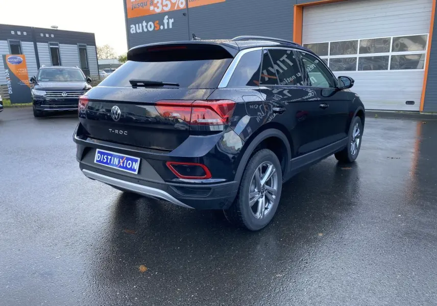 Volkswagen T-Roc noir en 3/4 arrière droit, avec vitres surteintées et jantes alliage visibles sur parking humide.