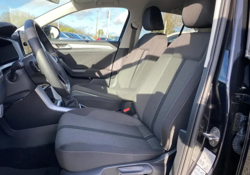 Vue intérieure côté conducteur du Volkswagen T-Roc noir 2025, montrant les sièges avant en tissu gris et le tableau de bord.