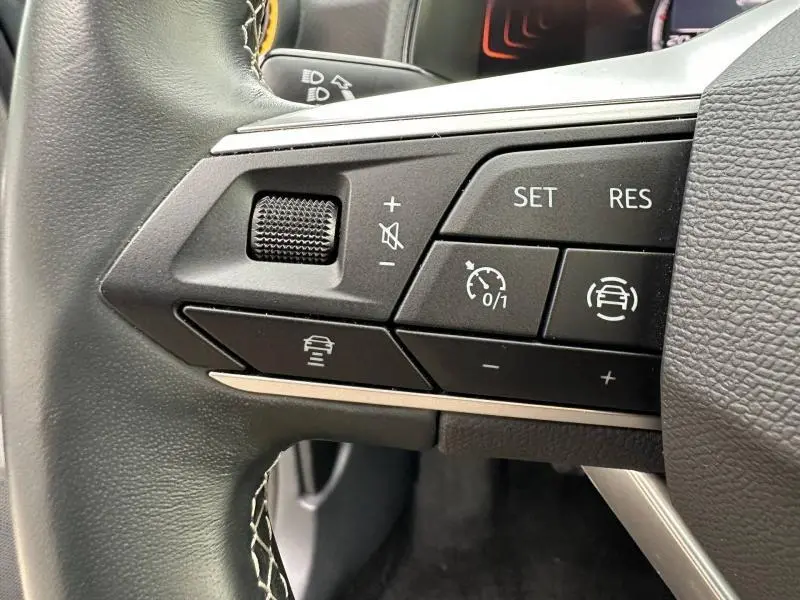 Gros plan sur les commandes de régulateur de vitesse au volant du SEAT Arona 2025, intérieur noir avec surpiqûres blanches.