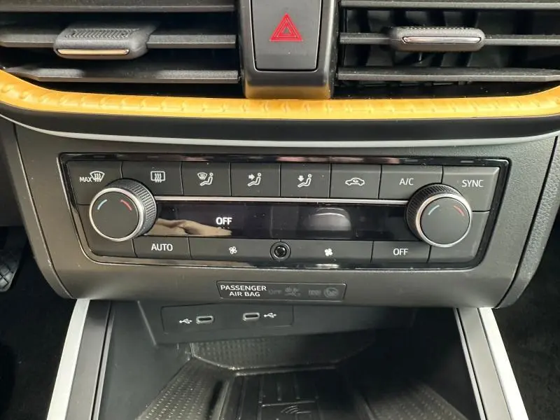 Vue rapprochée de la console centrale du SEAT Arona 2025, avec commandes de climatisation et bande décorative jaune.