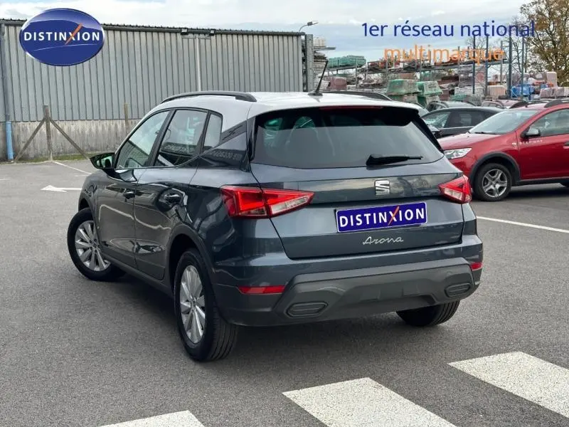 Vue 3/4 arrière d’un SEAT Arona 2025 gris Magnétique Métal avec toit blanc, garé sur un parking extérieur.