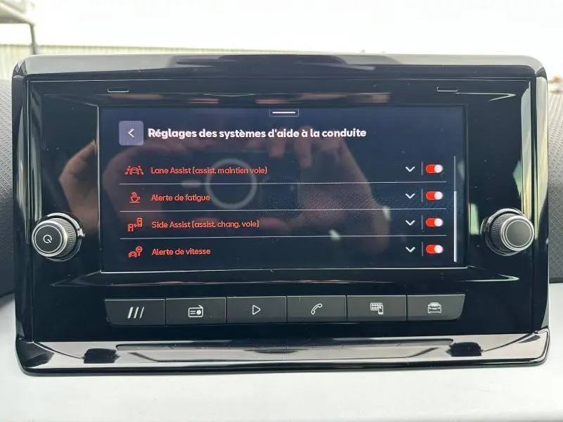 Écran tactile central du SEAT Arona 2025 affichant les réglages des aides à la conduite, entouré de boutons de commande noirs.