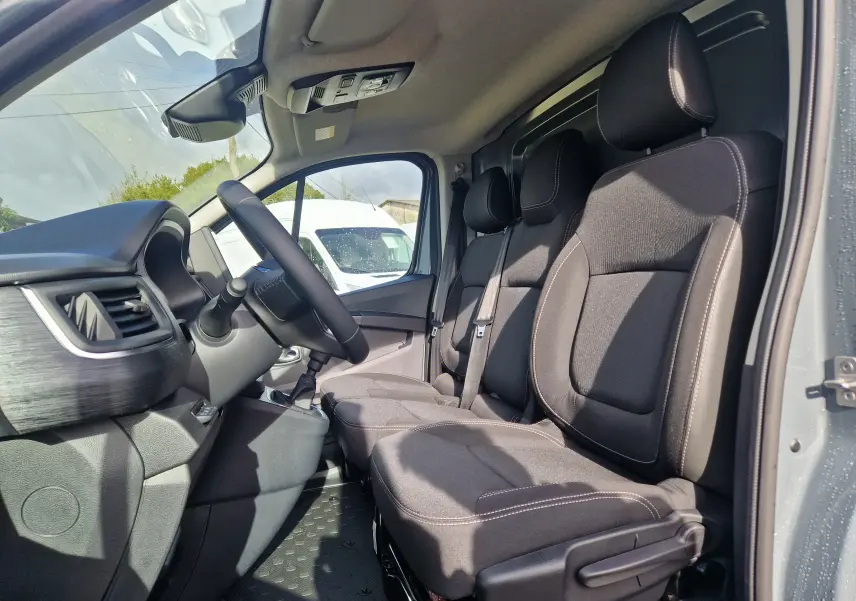 Vue intérieure côté conducteur du Nissan Primastar gris urbain 2025, montrant les sièges 3 places et le volant.