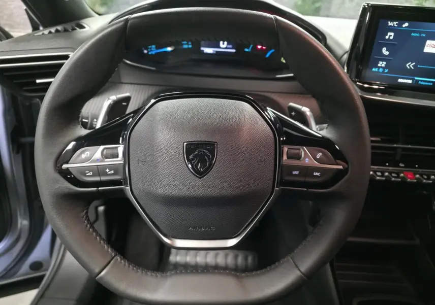 Vue rapprochée du volant compact cuir noir du Peugeot 2008 1.2i Hybrid 2025 avec commandes multimédia intégrées.